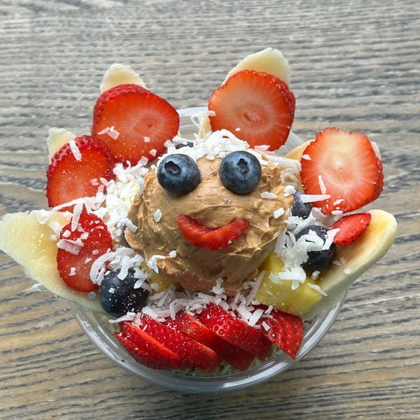 Aruba Island Bowls Cafe's acai bowl with a peanut butter face, blueberries, strawberries, and coconut flakes.