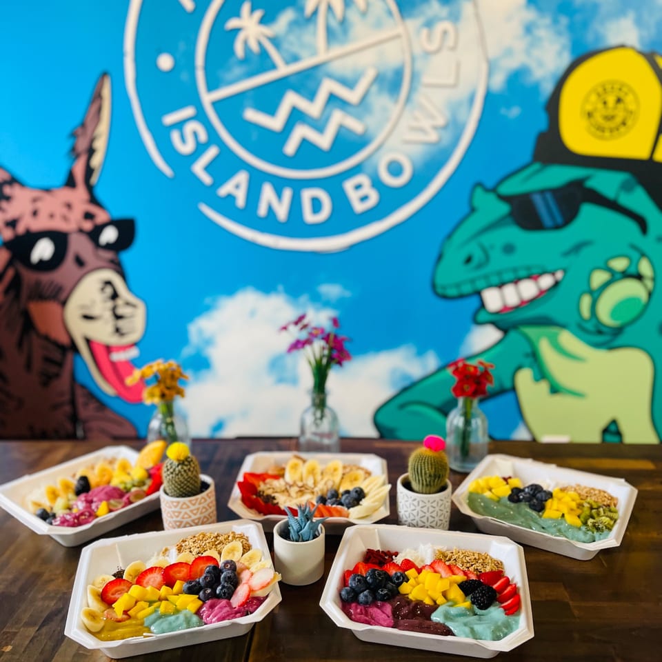 Five colorful Aruba Island Bowls acai bowls with fruit and toppings on a wooden table.