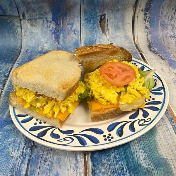 Scrambled egg and cheese sandwich with lettuce and tomato on a decorative plate.