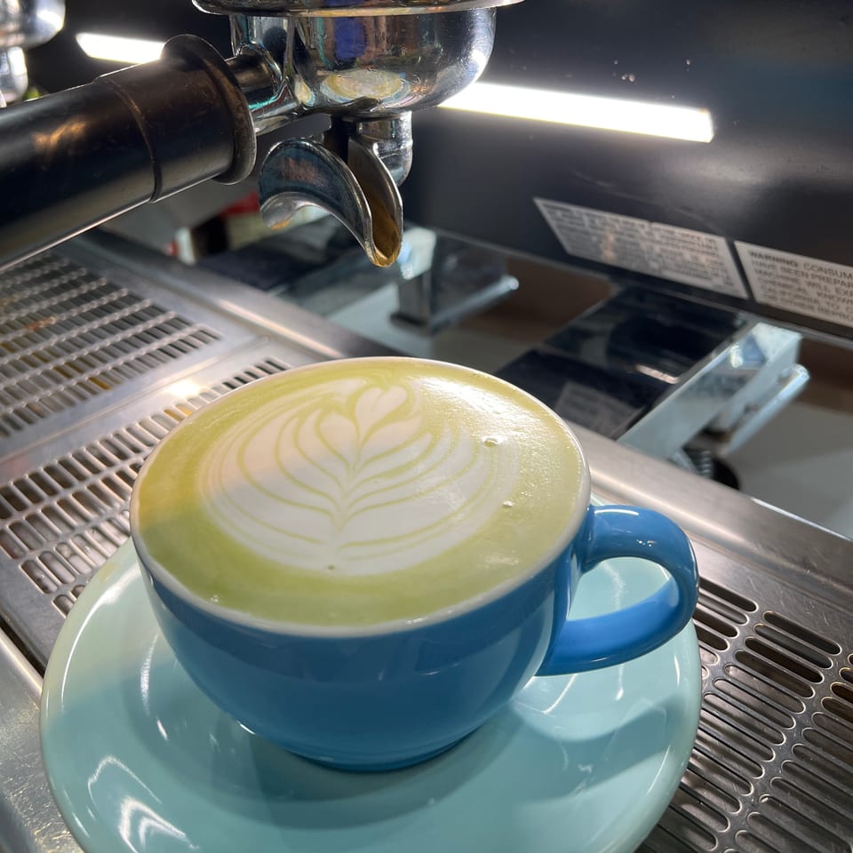 A vibrant green matcha latte with latte art in a blue cup on an espresso machine.