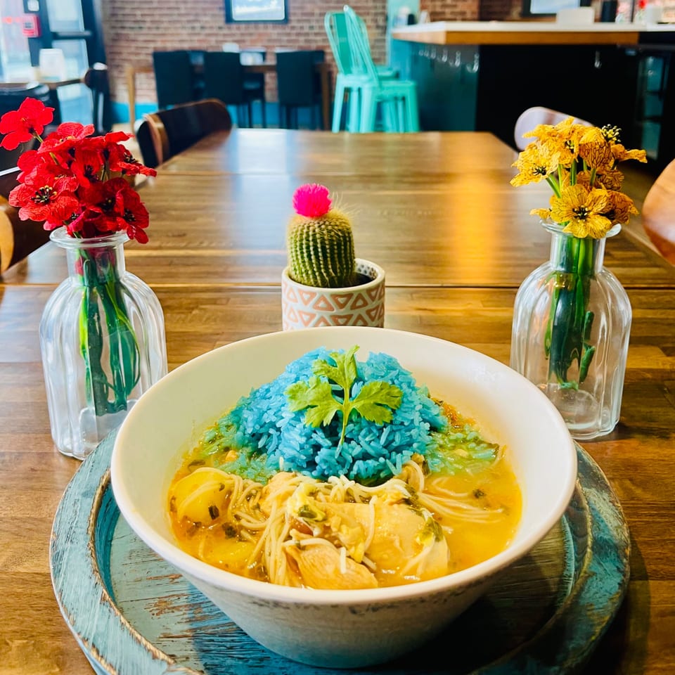 A vibrant blue rice dish with noodles and chicken, garnished with cilantro, on a wooden table.