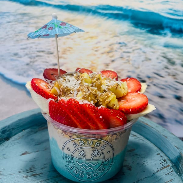 Aruba Island Bowls Cafe acai bowl with strawberries, pineapple, coconut, and a tiny umbrella.