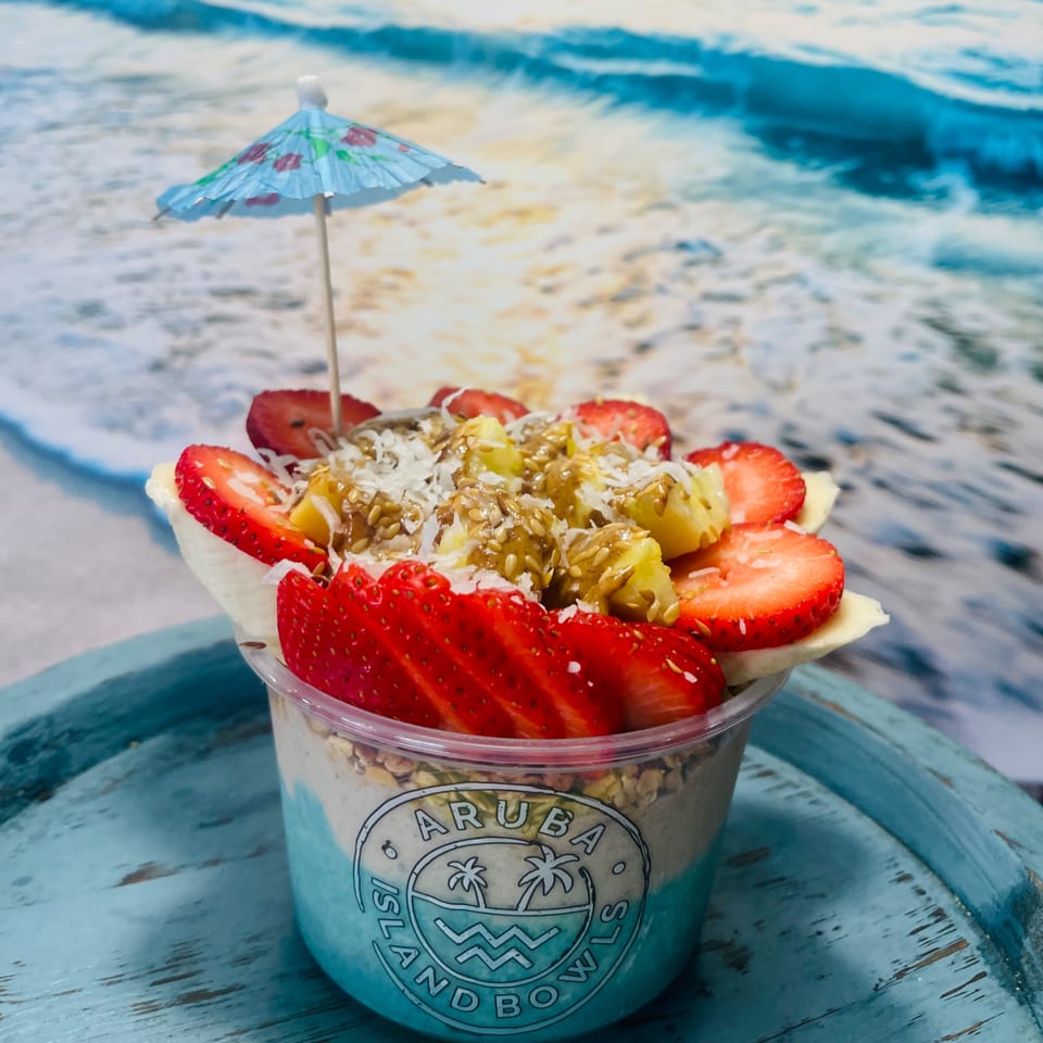 Aruba Island Bowls Cafe acai bowl with strawberries, pineapple, coconut, and a tiny umbrella.