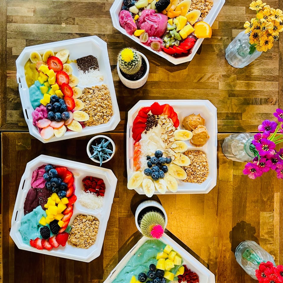 Overhead view of multiple colorful acai bowls with various fruits, granola, and toppings on a wooden table.