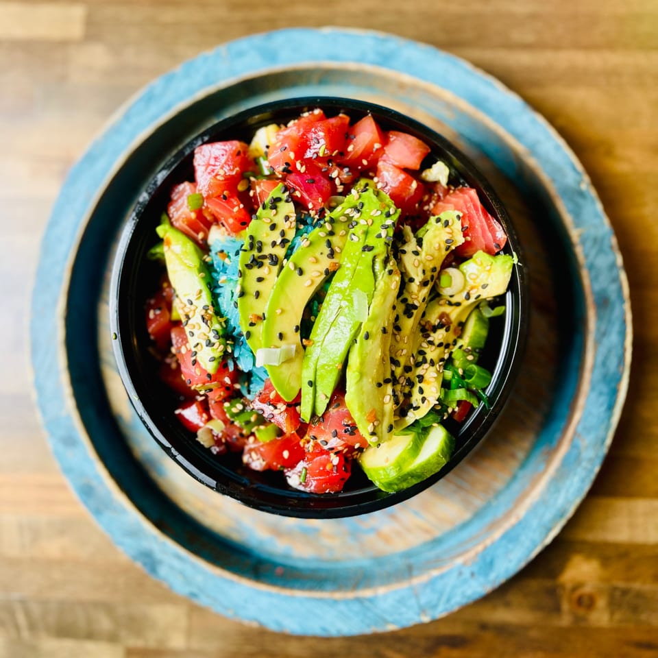 Colorful poke bowl with tuna, avocado, and sesame seeds on a blue-rimmed plate.