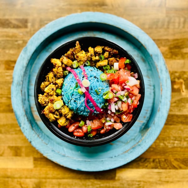 A colorful Aruba Island Bowls Cafe bowl with blue rice, chicken, salsa, and beans on a blue tray.