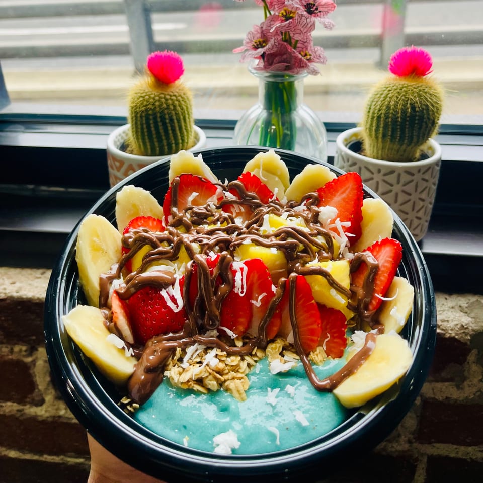 A vibrant blue acai bowl topped with bananas, strawberries, pineapple, granola, and chocolate drizzle.
