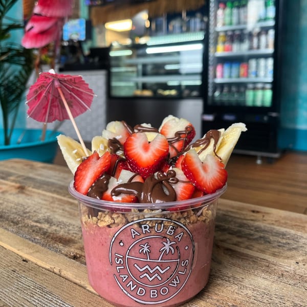 Aruba Island Bowls Cafe acai bowl with strawberries, bananas, chocolate drizzle, and a pink umbrella.