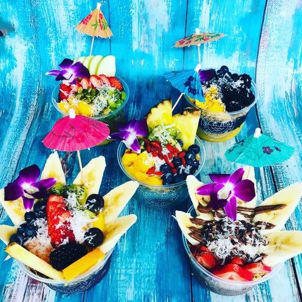 Five vibrant Aruba Island Bowls, garnished with fresh fruit, orchids, and tiny umbrellas on a blue wooden surface.