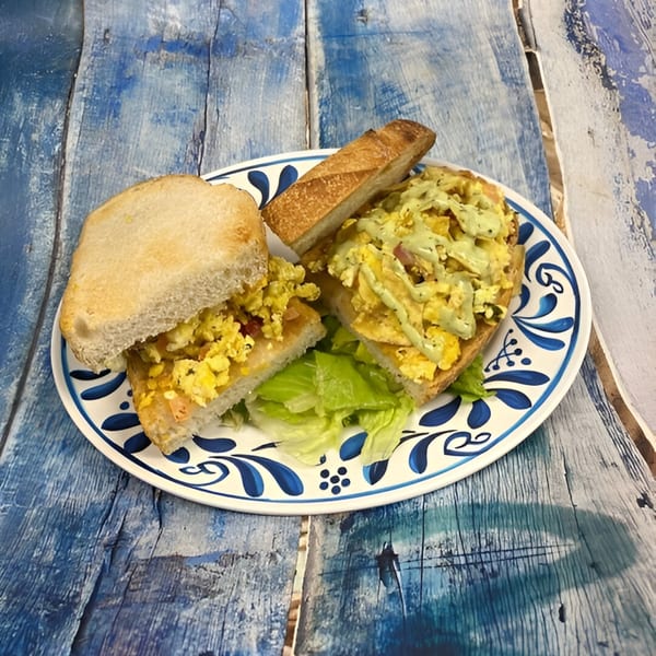 Scrambled egg sandwiches with green sauce and lettuce on a blue and white plate.